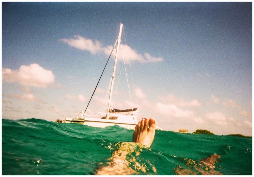 A person floating in turquoise water near a sailbo