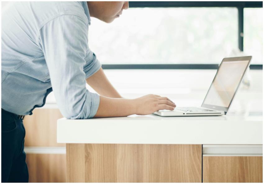 A man leaning on a desk working on a laptop in a b