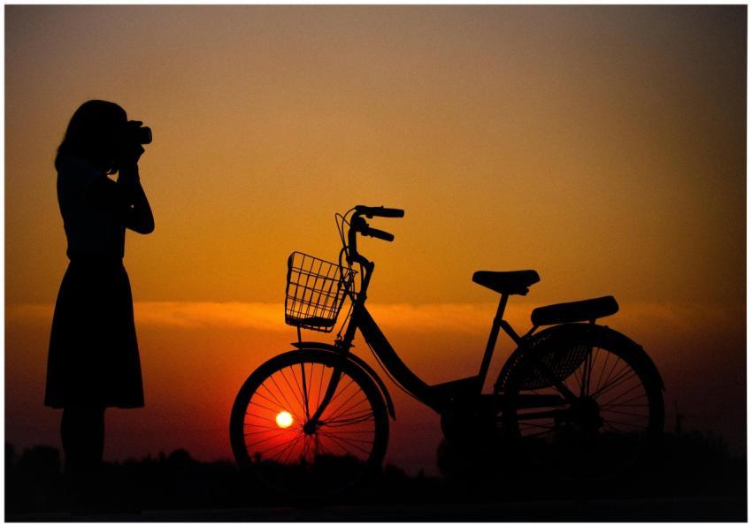 A silhouette of a woman photographer and a bicycle