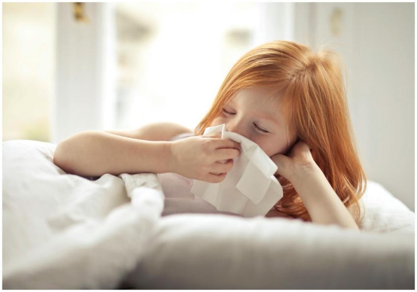 Redheaded child resting in bed, wiping nose with t