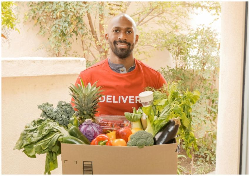 Deliveryman in red shirt holding a box of fresh ve