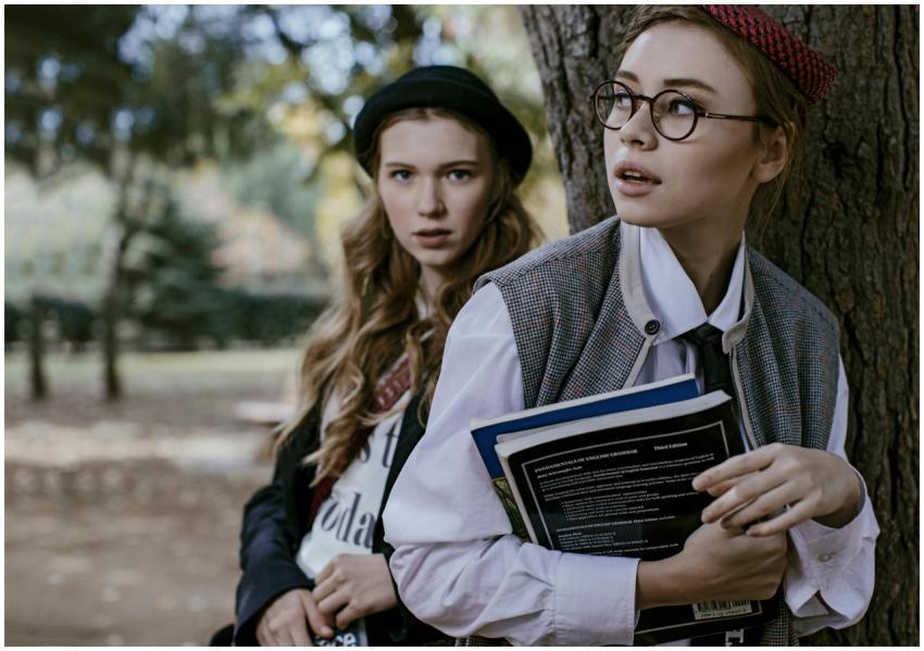 Two stylish young women outdoors, holding books, w