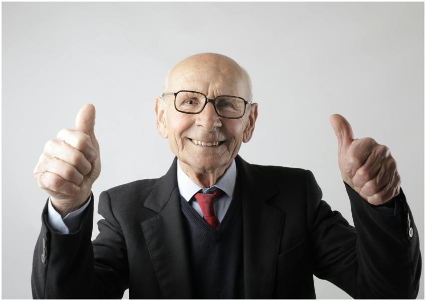 Cheerful elderly man in suit giving thumbs up, sym