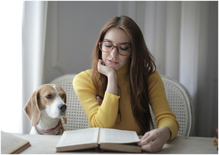 Young woman reading a book with her dog beside her