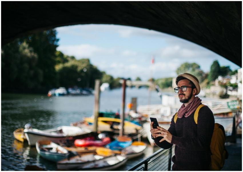 A man with a hat and scarf using smartphone by a s