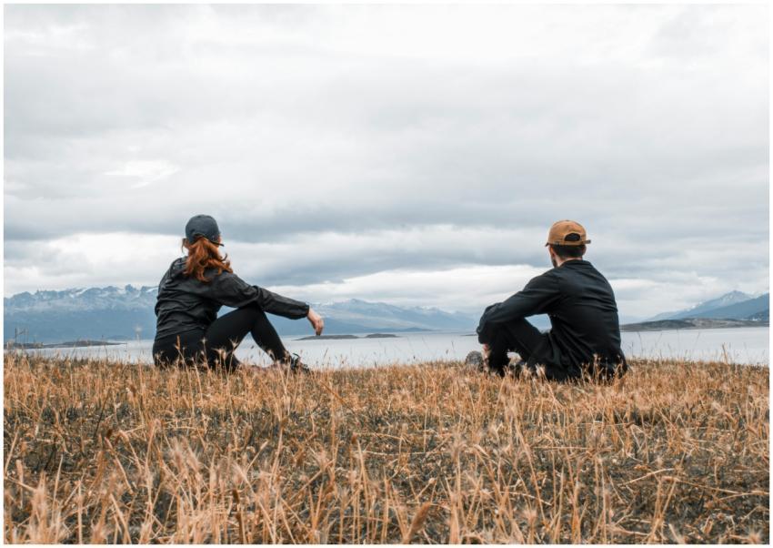 Couple sitting on grass, admiring a lake in Ushuai