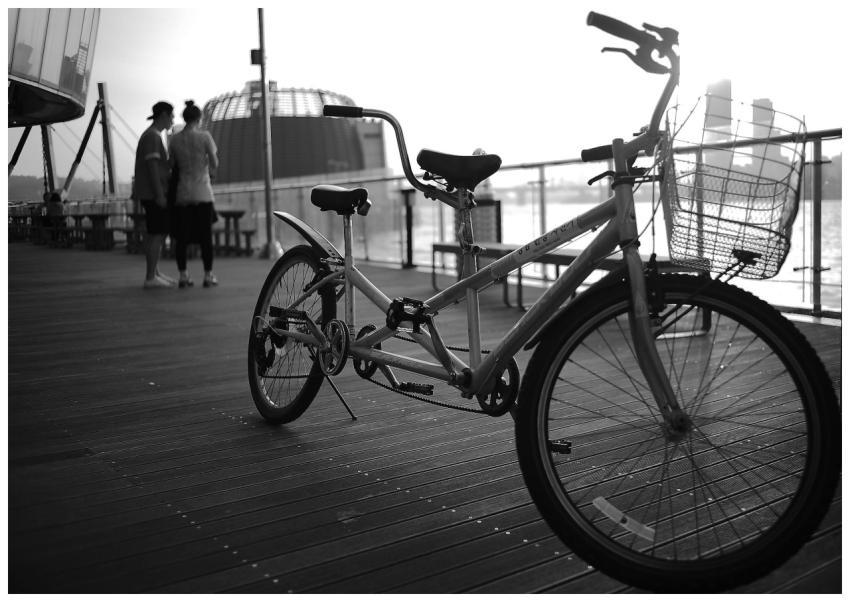 A tandem bicycle on a pier at sunset with two peop