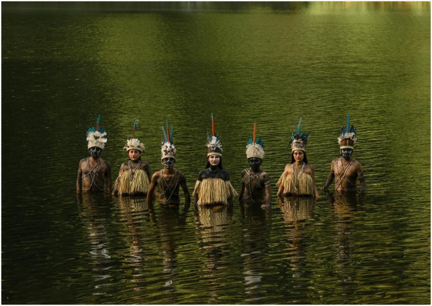 Tribal members in traditional attire stand in wate