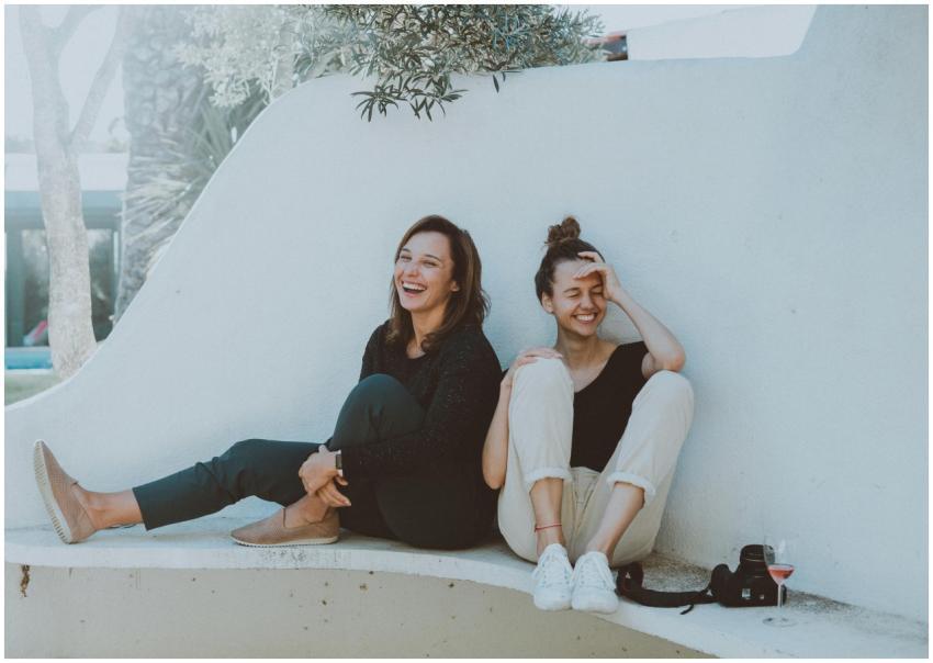 Two women laughing together outdoors, enjoying lei