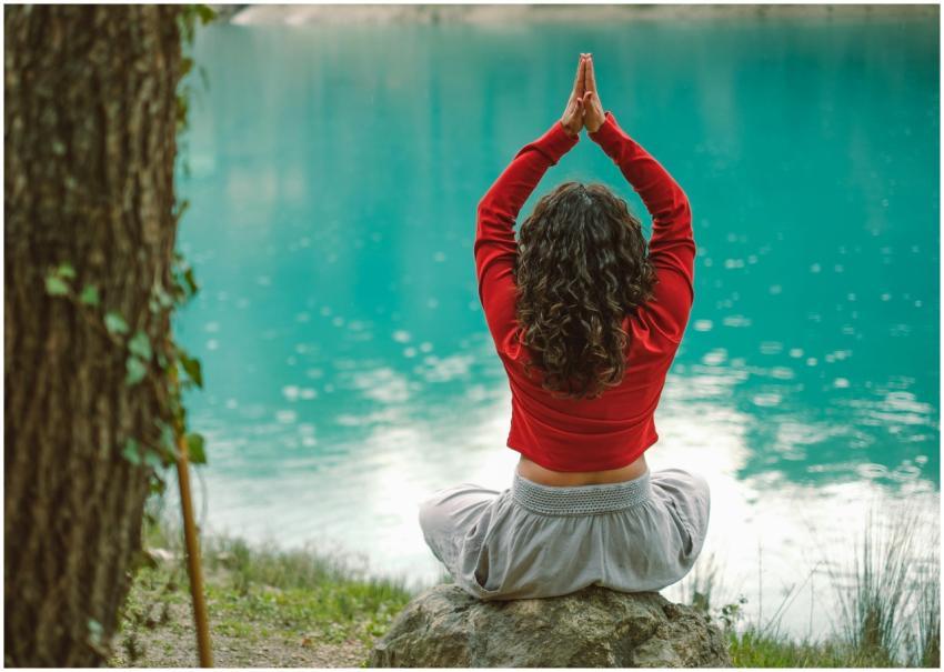 A woman meditates in nature on a rock by a tranqui