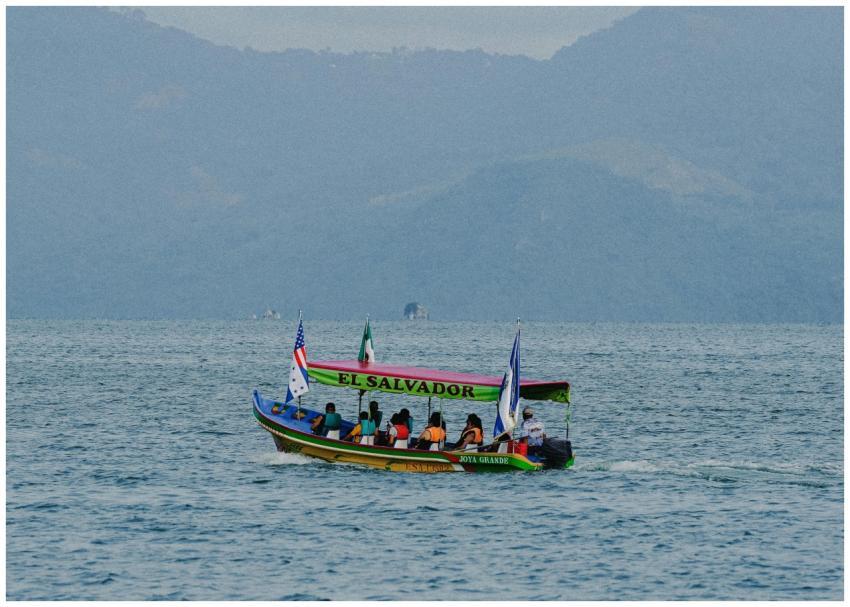 A colorful boat with flags sails on a serene lake