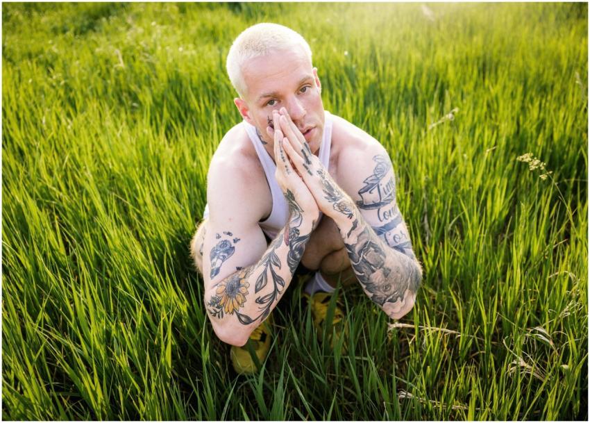 A man with tattoos and dyed hair squatting in a su