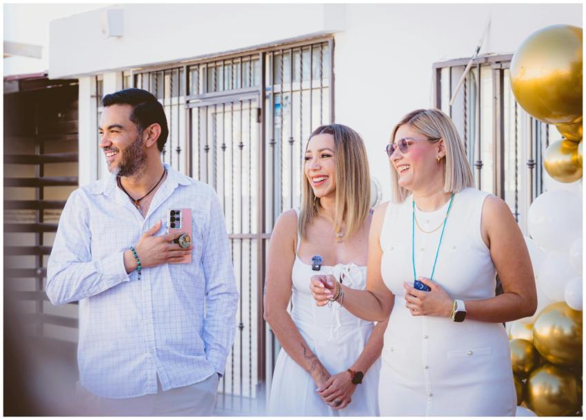 Three adults smiling at an outdoor celebration wit