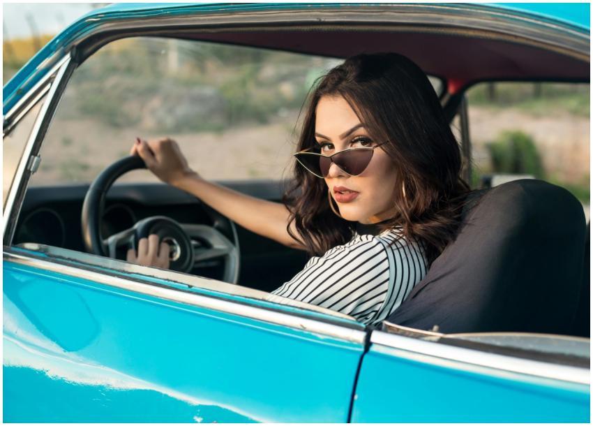Woman in sunglasses driving a vintage blue car on