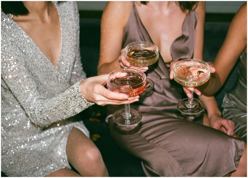Three women in stylish dresses toasting with champ