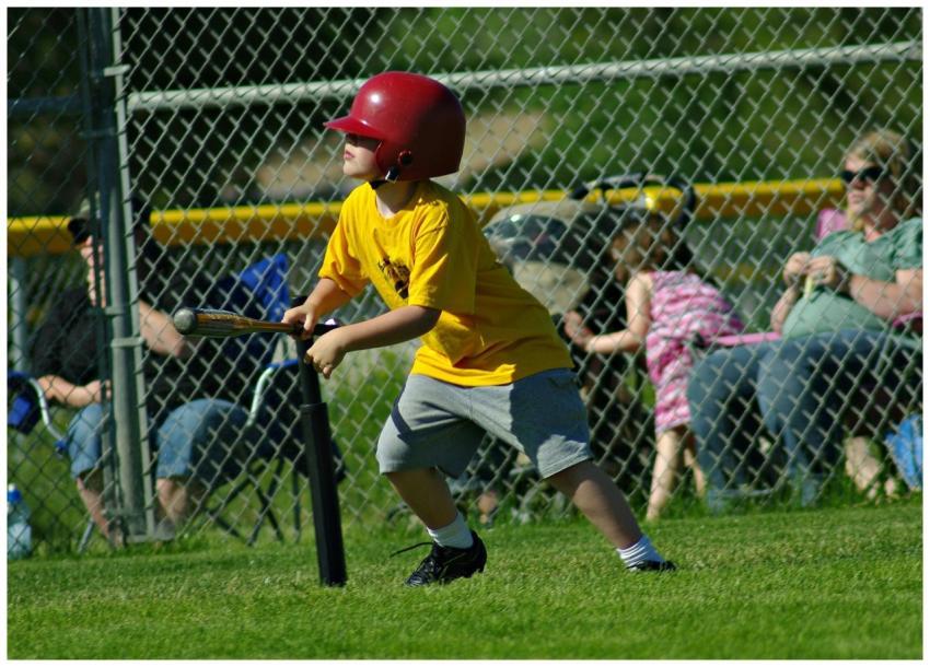 Child in a yellow shirt and helmet playing basebal