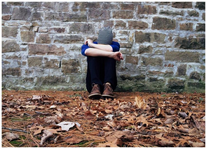A solitary figure sits against a stone wall surrou