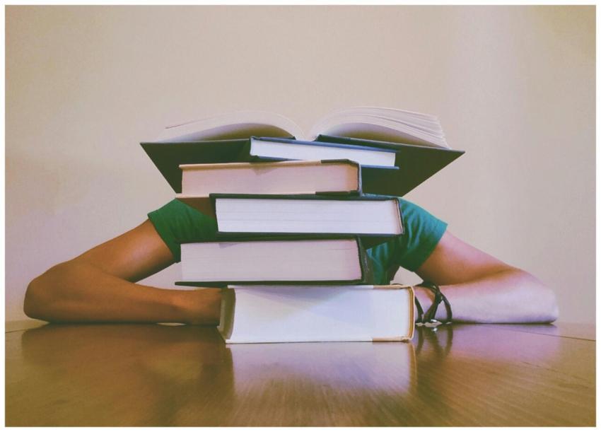 A student hidden behind a stack of books, symboliz