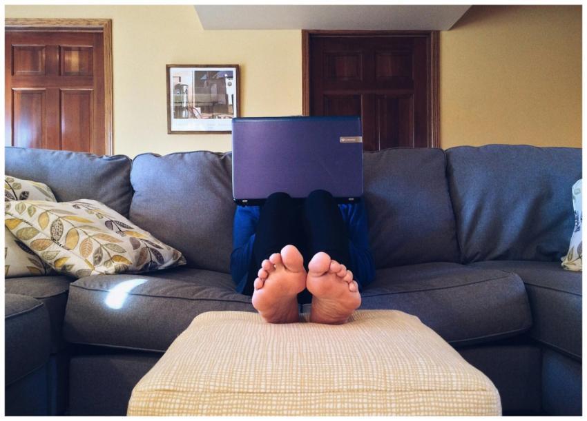 Person relaxing on a cozy couch with a laptop, emb