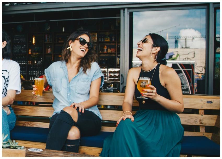 Two women laughing and enjoying drinks outdoors at