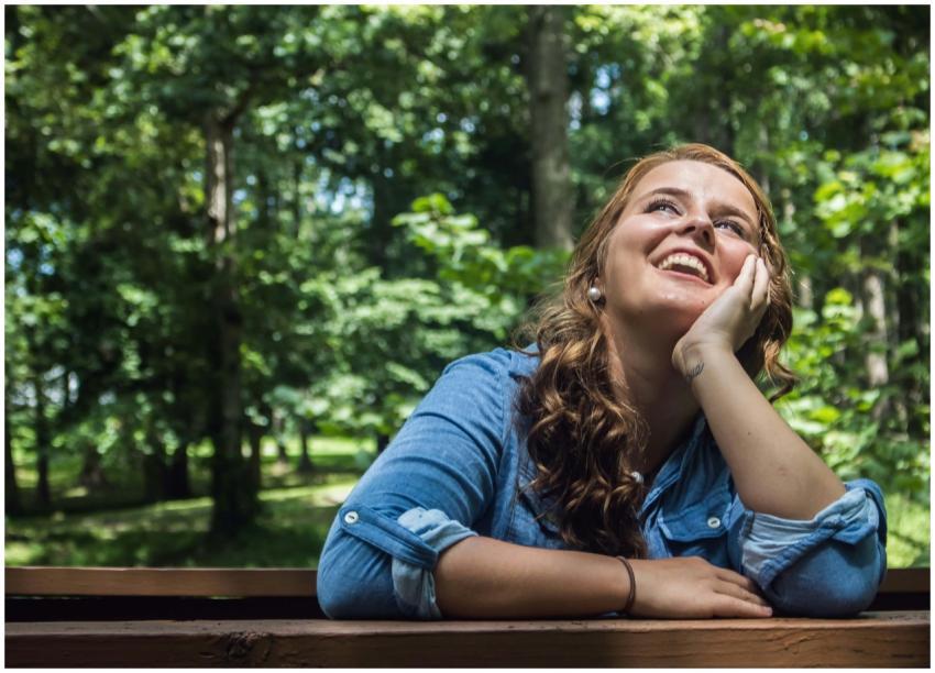 A smiling woman in a park leaning on a wooden rail