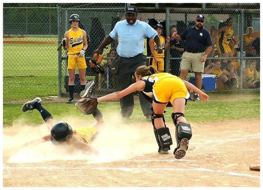 Youth softball player slides into home plate as th