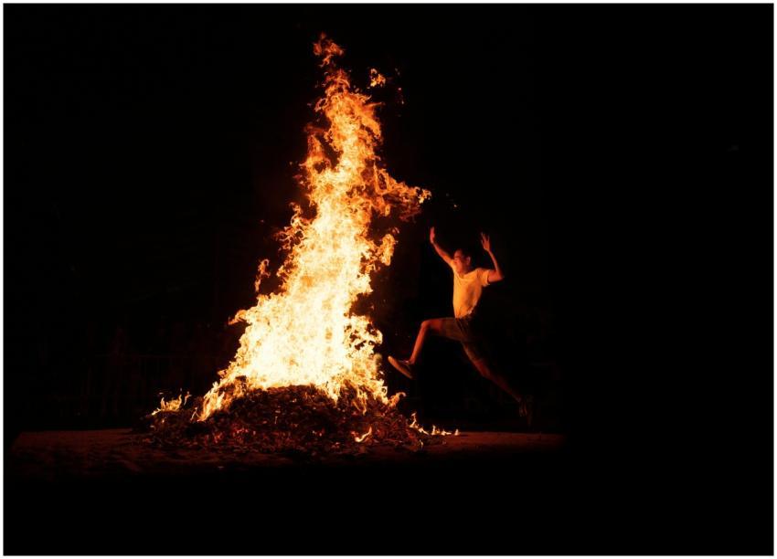 An adventurous man leaps over a large bonfire duri