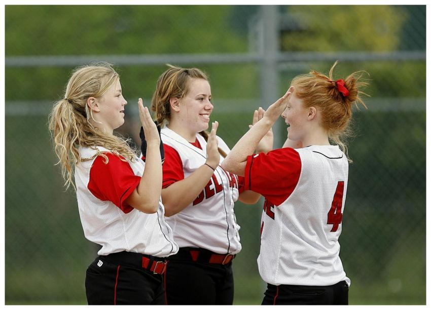 Teen girls in softball uniforms celebrating a vict