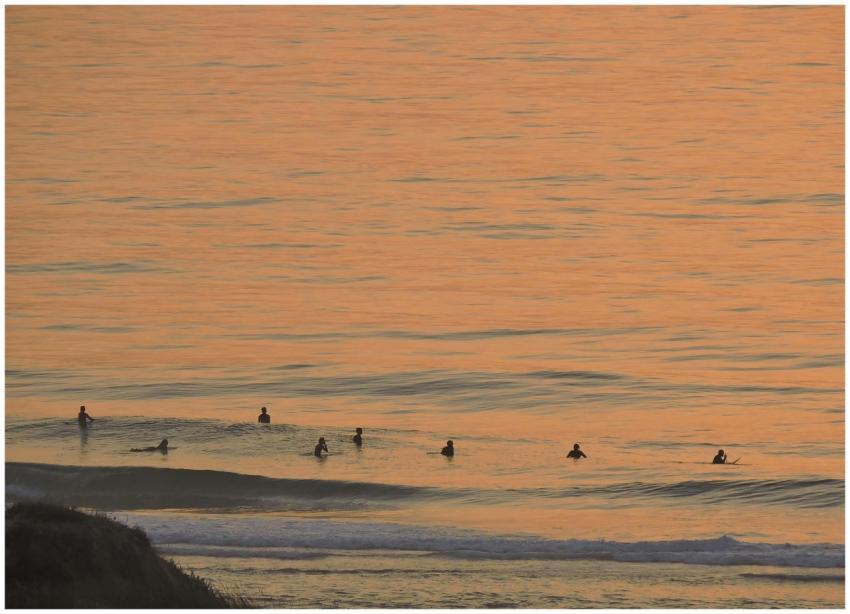 Surfers enjoying a serene sunset on calm ocean wav