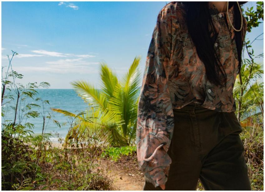 A woman in a floral shirt walks by the ocean with