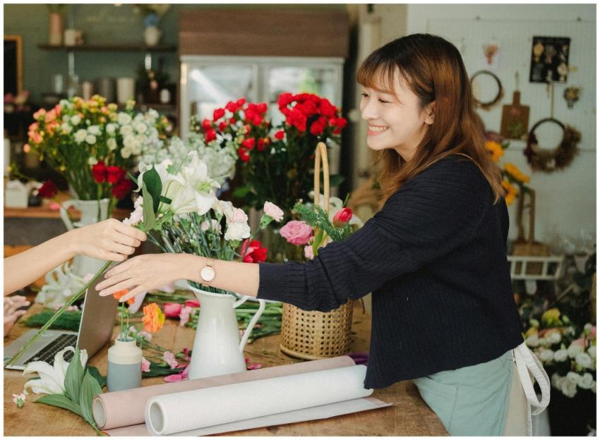 Side view of happy female in apron arranging flowe