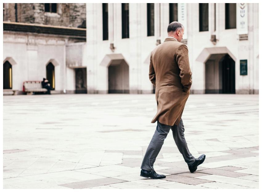 A man in a coat walks through a modern city plaza,