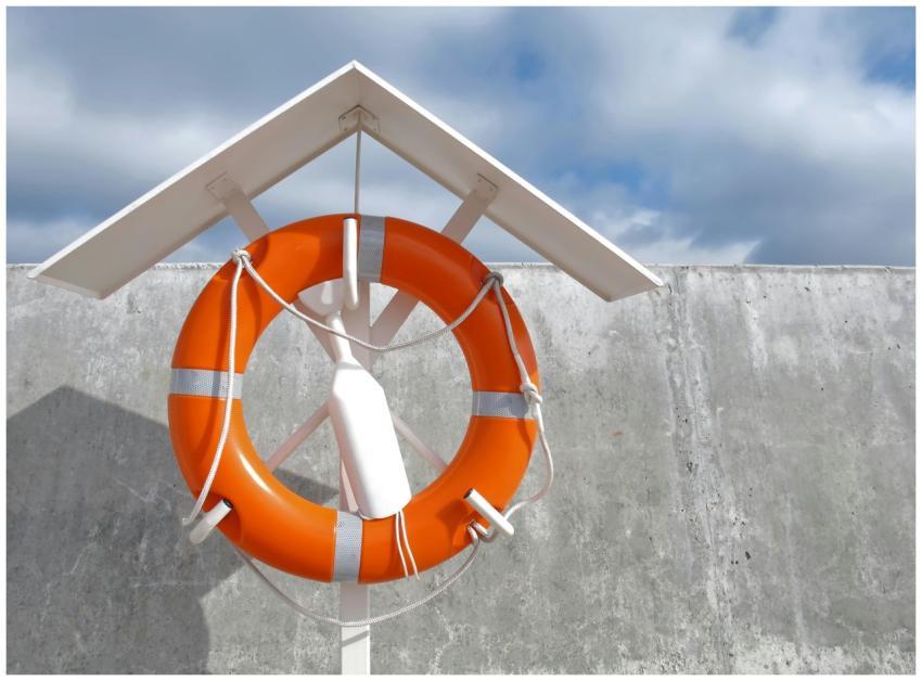 A vibrant orange lifebuoy hangs on a concrete wall