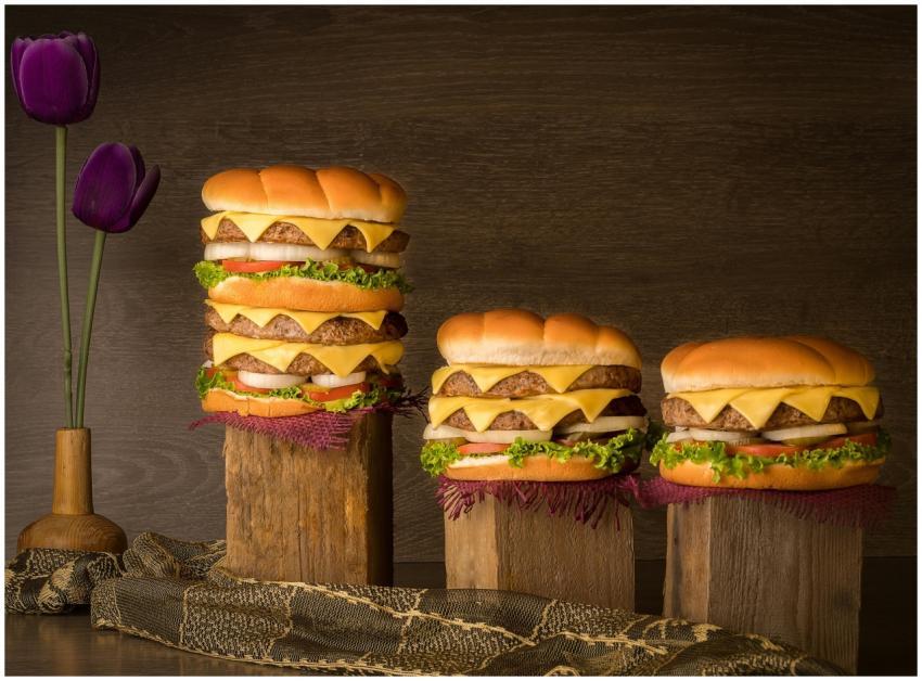 Three stacked cheeseburgers with wooden backdrop a