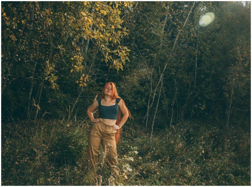 A woman with red hair poses confidently in a lush