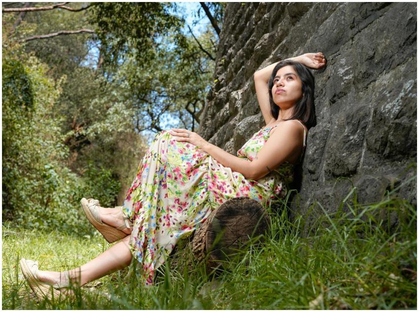 Young woman in floral dress resting against a ston