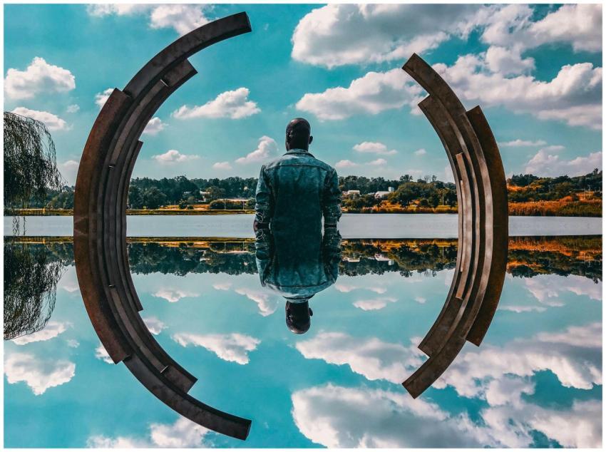 A man in a denim jacket sits by abstract sculpture