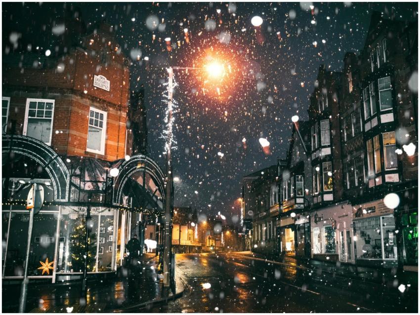 Magical night scene with snow falling on a lit urb