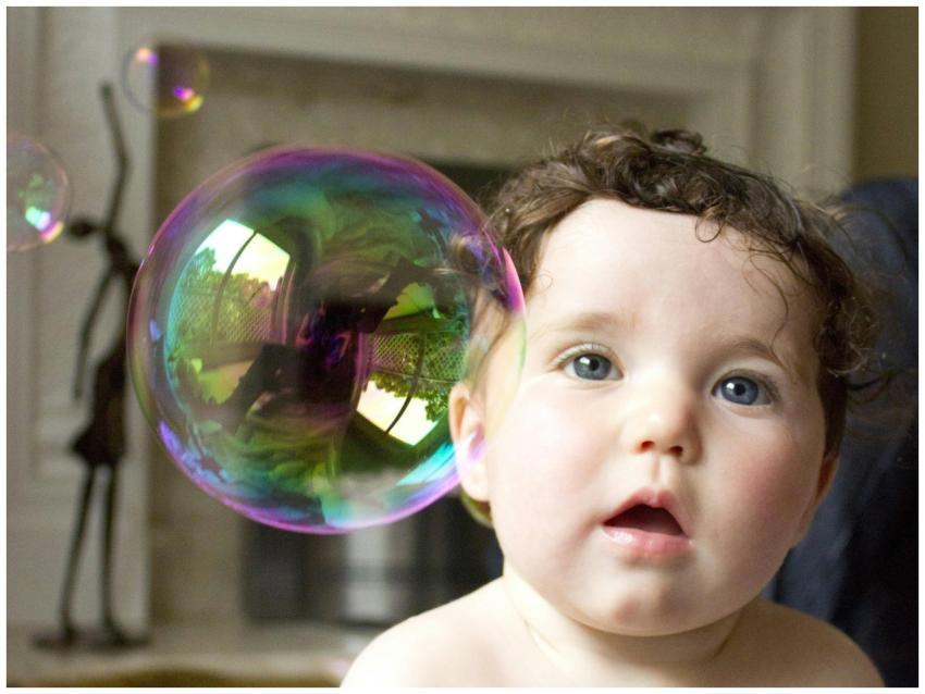Cute baby looking at a large colorful bubble indoo