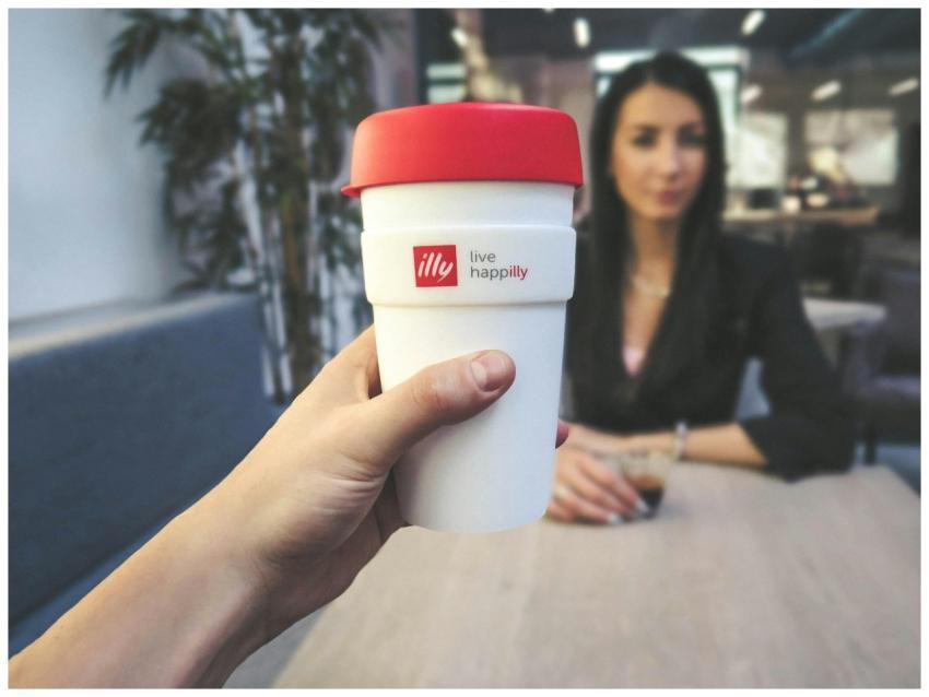 Focus on a reusable coffee cup with a woman in a b