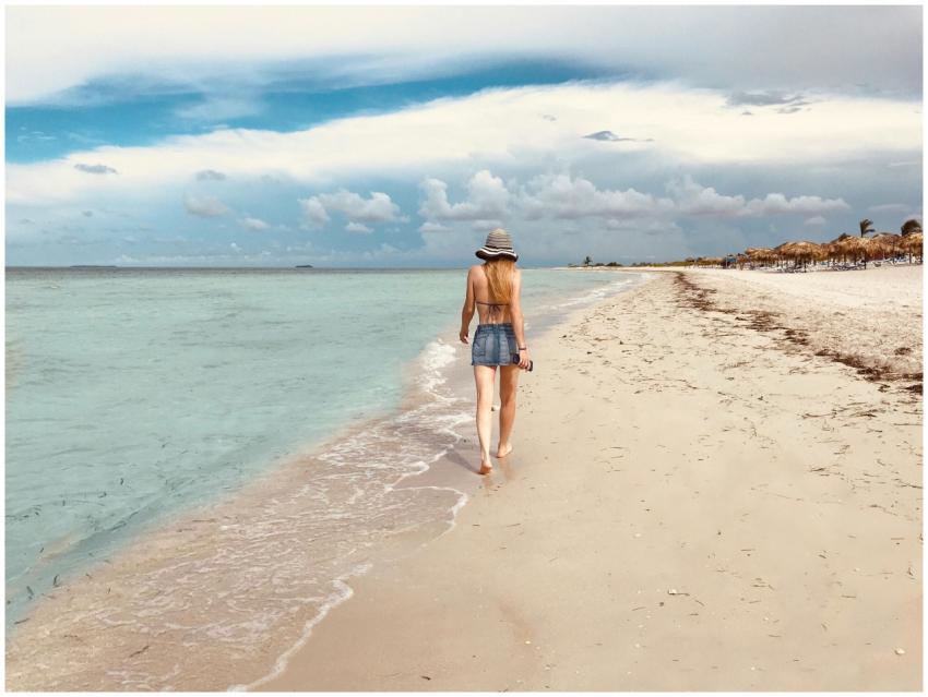 A woman walks along a serene tropical beach, enjoy