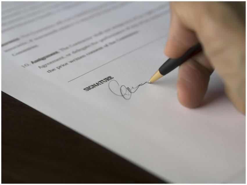 A hand signs a formal contract with a pen on a woo