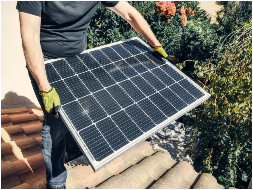 A worker in gloves installs a solar panel on a til