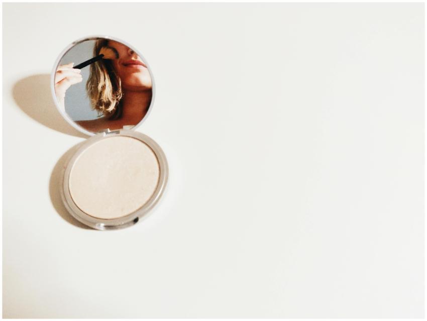 Close-up of a woman using makeup in a compact mirr