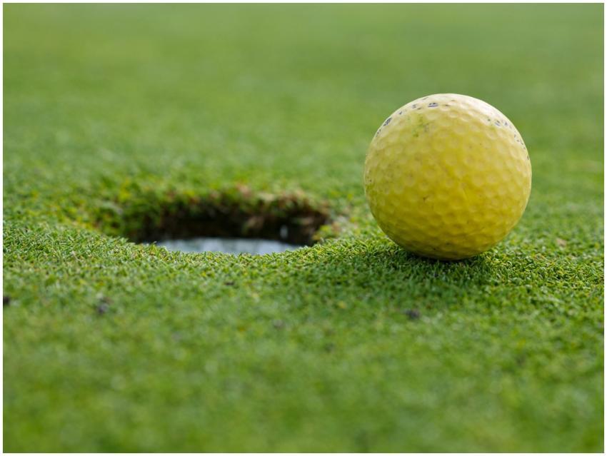 A yellow golf ball close to the hole on a grassy g