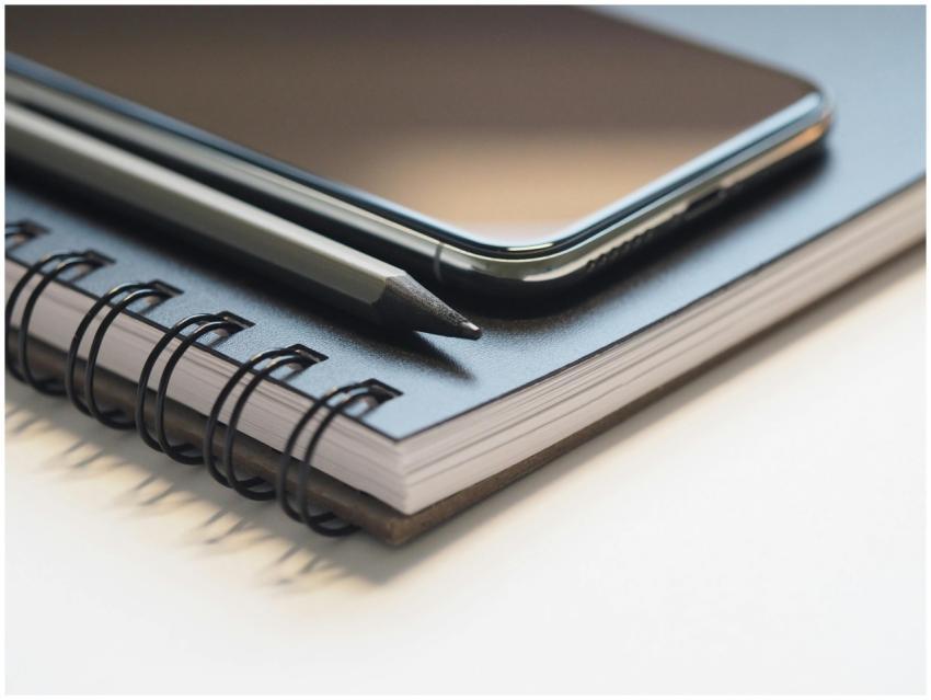Close-up of a spiral notebook, smartphone, and pen