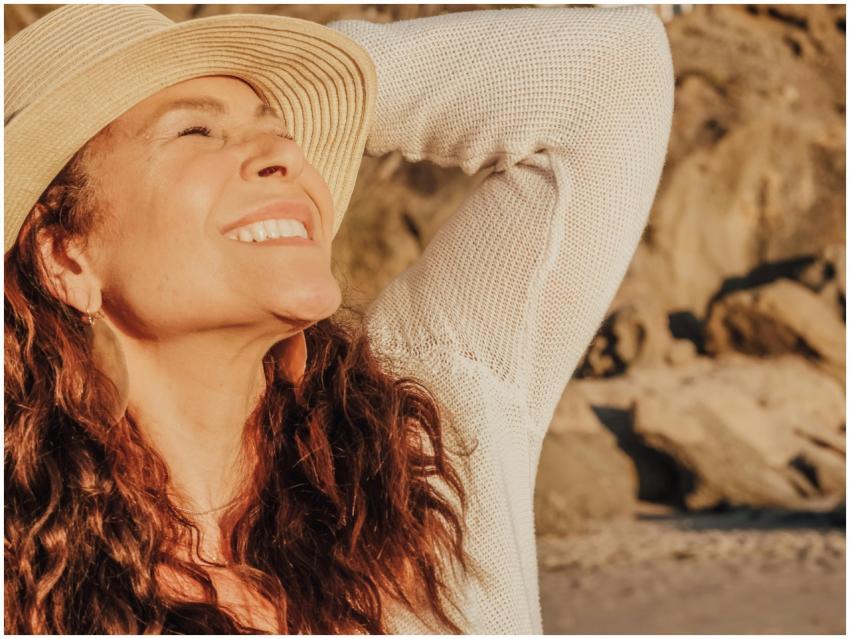 A joyful woman with a hat basks in the sunlight by