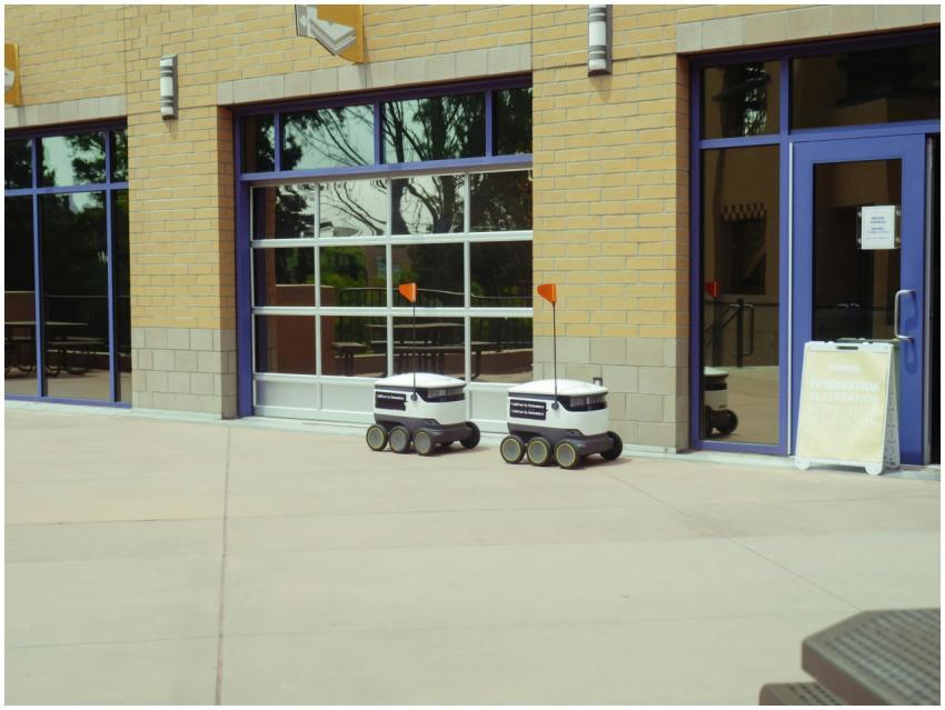 Two autonomous delivery robots navigate an outdoor