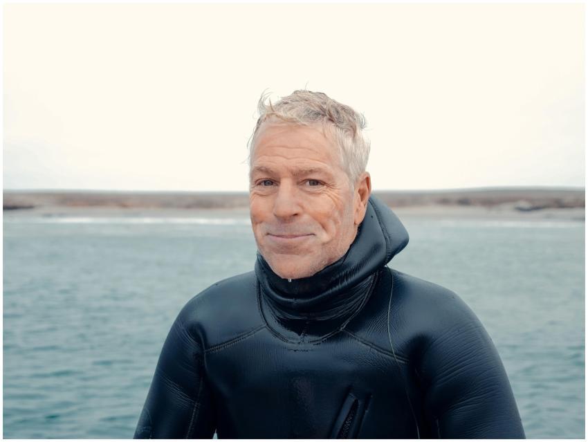 Happy elderly man in a scuba wetsuit standing by t