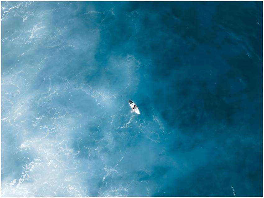 Drone shot capturing a lone surfer riding the ocea